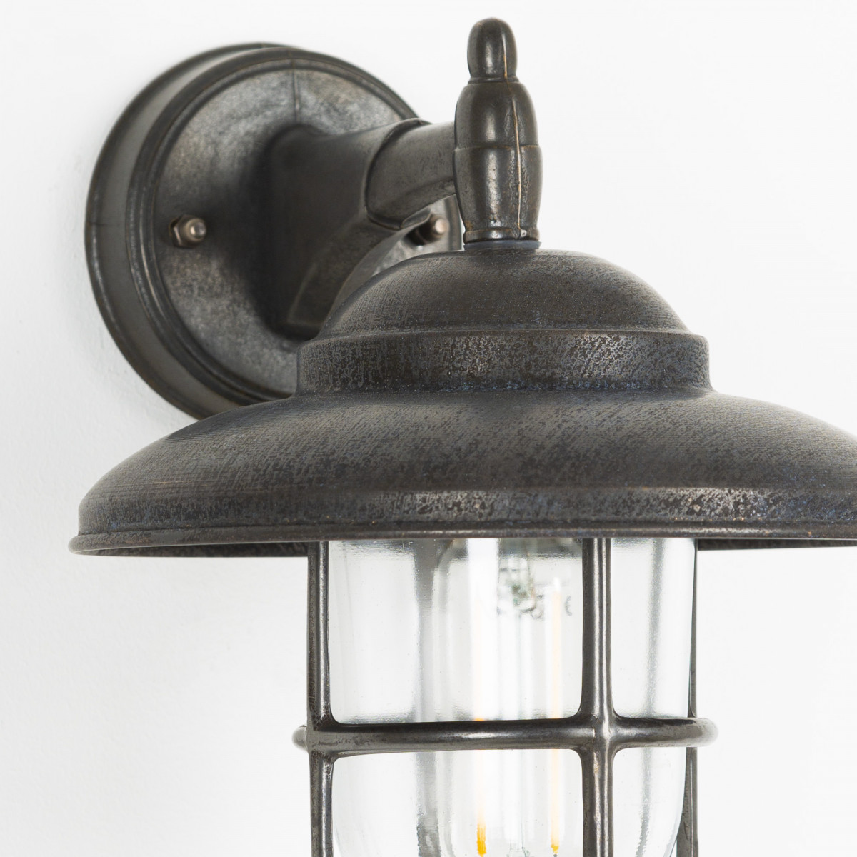 Monte wandlamp in antiek zwart met metalen kap, helder stolpglas en beschermend raster,E27 fitting, IP54-classificatie.