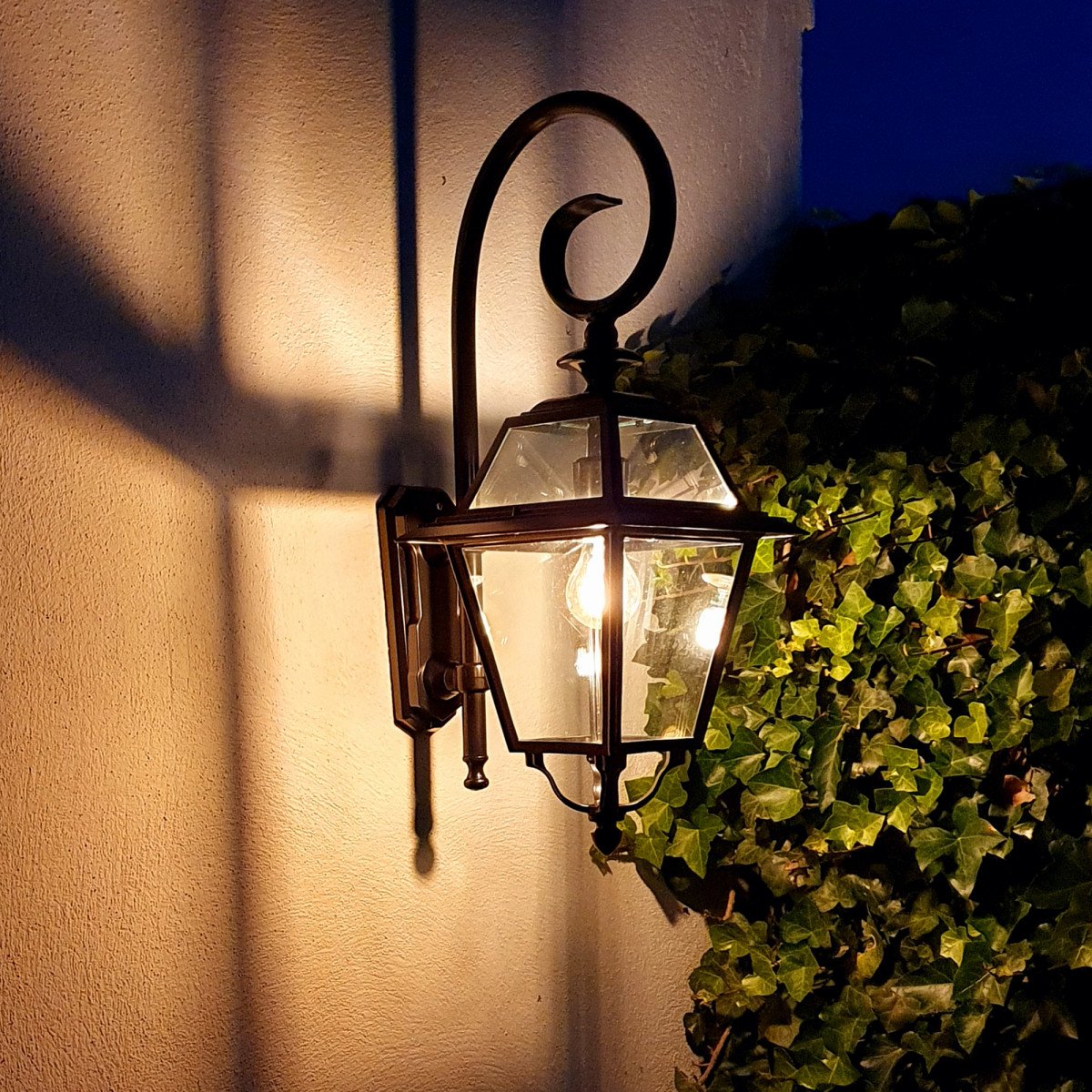 Buitenlamp Amstelrade, strak klassiek vormgegeven zwarte wandlantaarn met heldere beglazing, stijlvolle wandsteun met grote krul, gevel verlichting