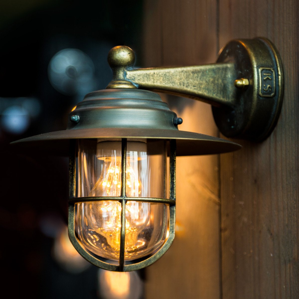 Bronzen wandlamp Labenne met helder stolpglas, beschermend raster en koperen kap – duurzame buitenverlichting van KS.
