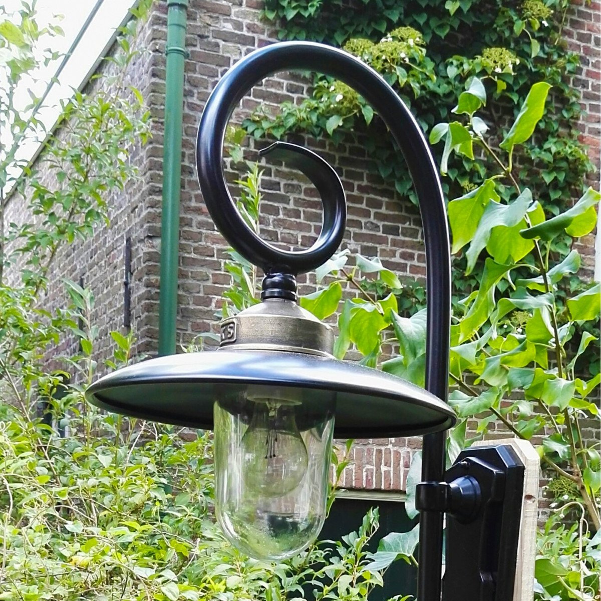 Buitenlamp Orly met sierlijke krularm, zwarte aluminium kap, bronzen flens en glazen stolp,  Wandlamp in Franse stijl.