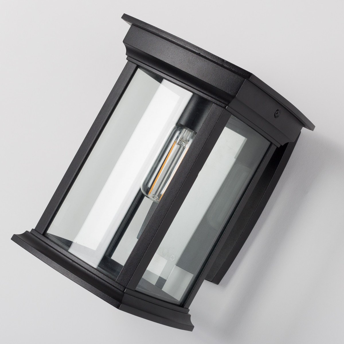 Zwarte wandlamp voor buiten, vierkante muursteun, lantaarnkap met zwart frame en heldere ruitjes, lichtbron boven in de kap, zichtbaar in het armatuur