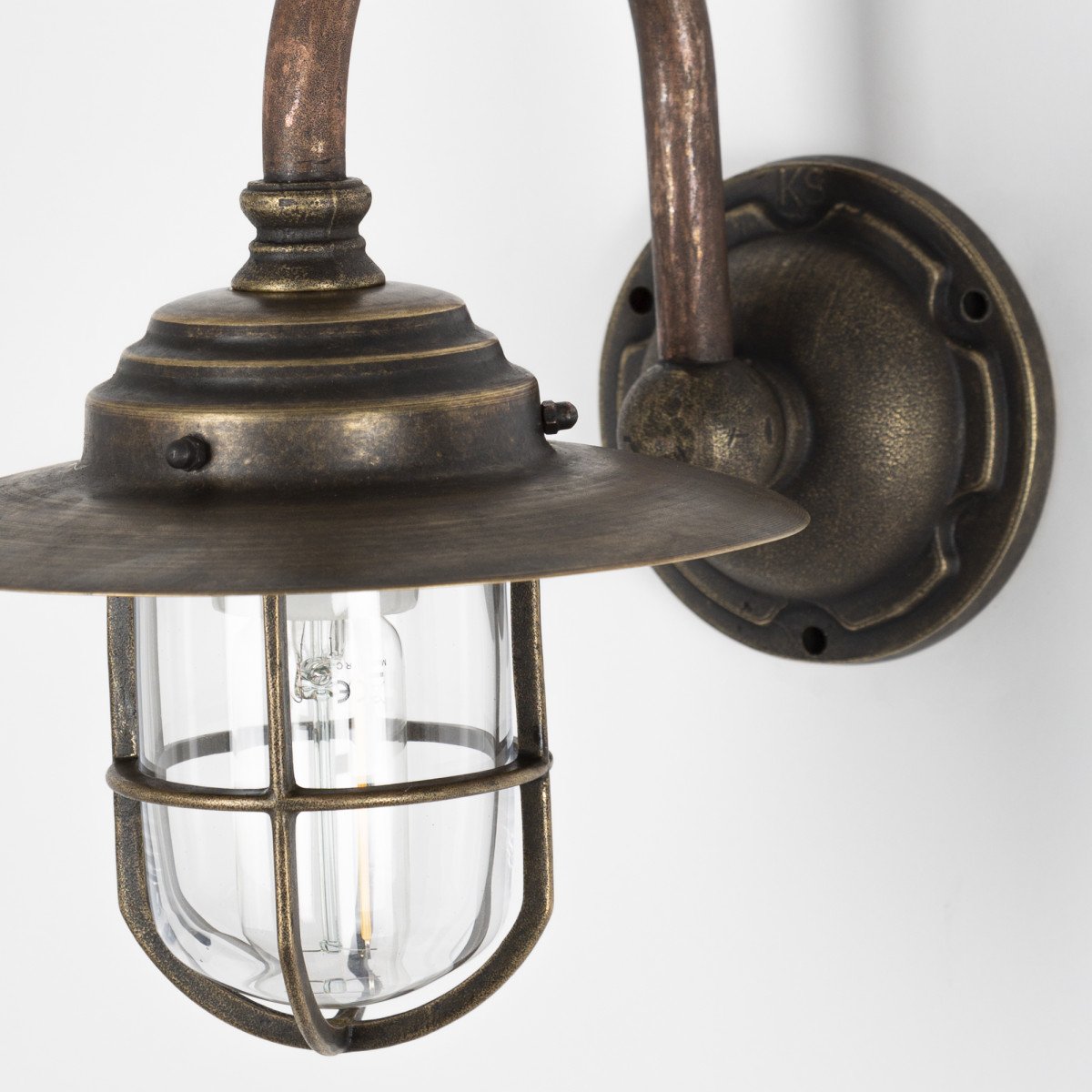 Klassieke wandlamp Barro met bronzen muurplaat, koperen kap, boogarm, raster rond helder stolpglas, duurzame verlichting