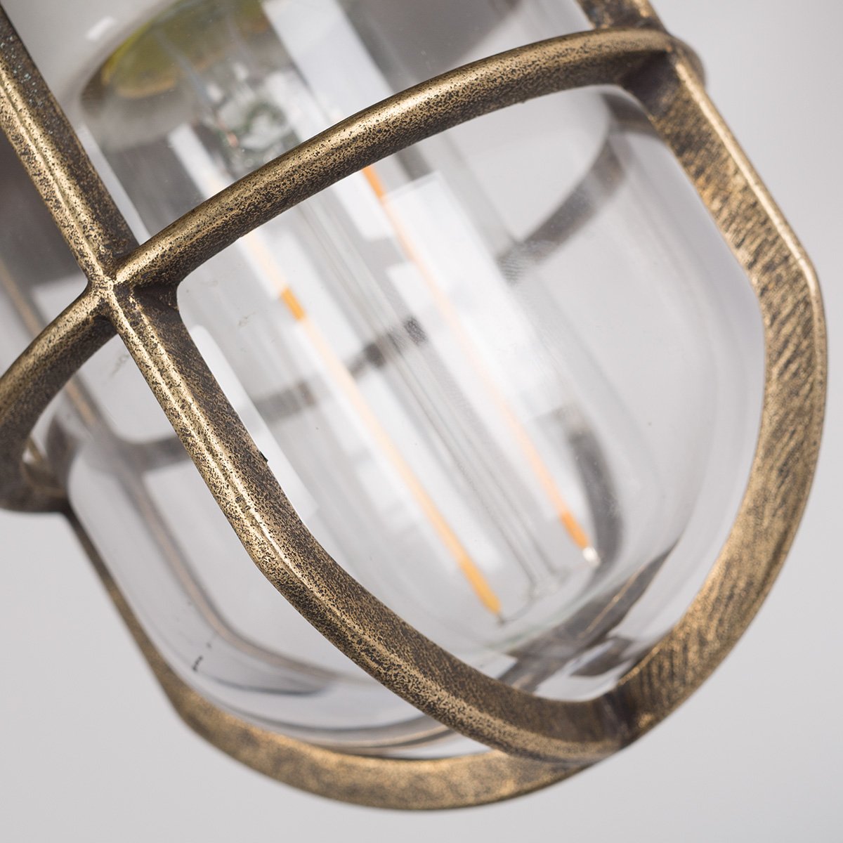 Buitenlamp Tour met bronzen wandarm, koperen kap, helder stolpglas en beschermend raster.