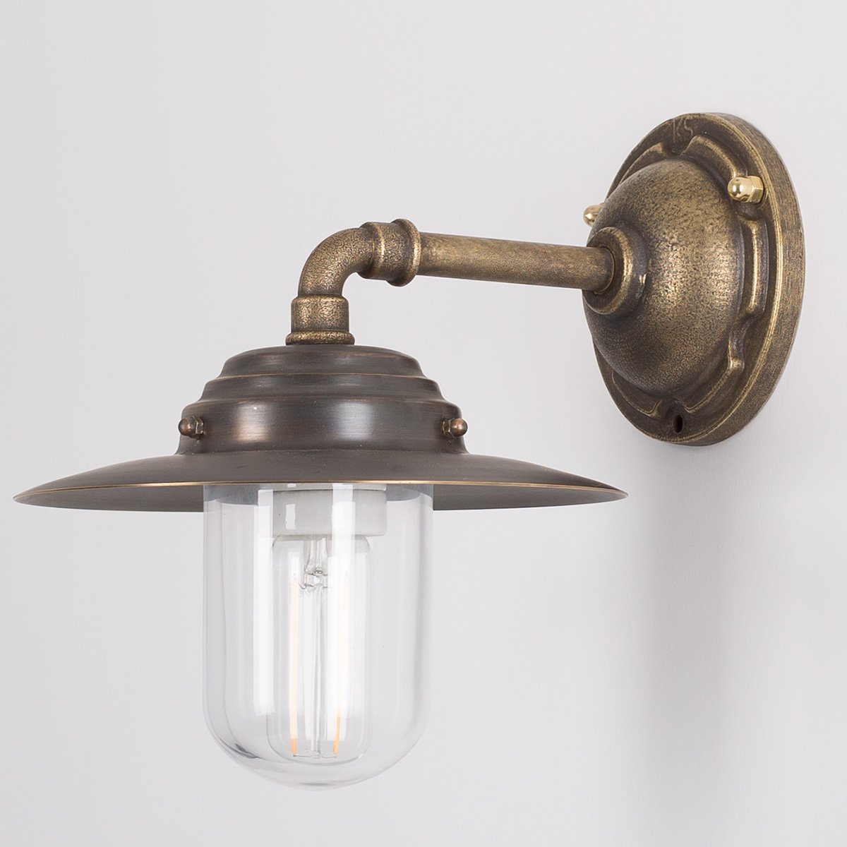 Stoere bronzen buitenlamp Dijon met compacte wandarm, helder stolpglas geschikt voor gevelmontage.